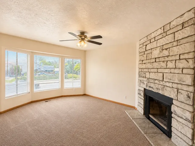Living space featuring a stone-clad fireplace with a hearth, a multi-pane bay window, and a ceiling fan with integrated lighting