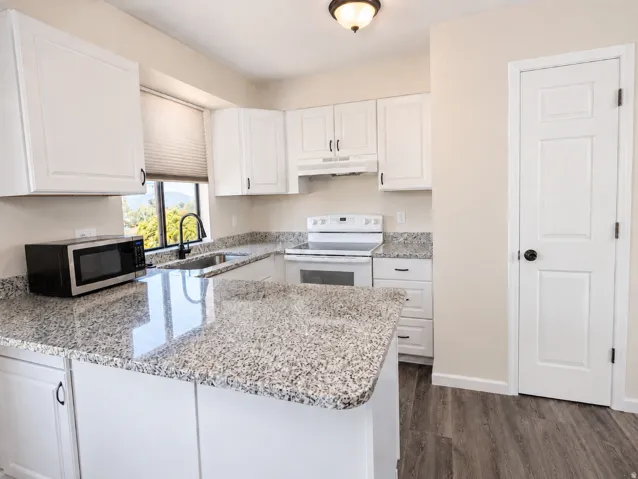 Modern kitchen featuring white cabinetry, speckled countertops, a double basin sink with a gooseneck faucet, a white range, and wood-finish flooring