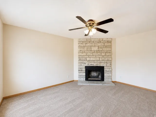 Living space featuring a stone-clad fireplace with a hearth, a dark metal firebox, and neutral-toned wall-to-wall carpeting