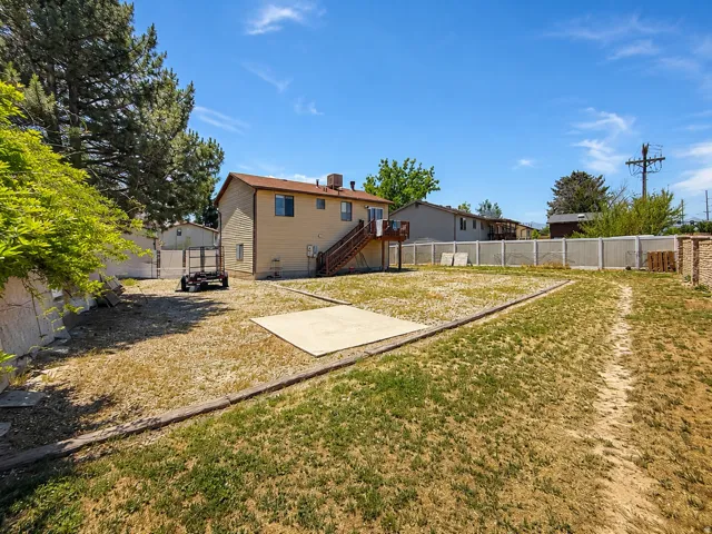 Expansive backyard featuring a concrete patio, perimeter fencing, and mature trees