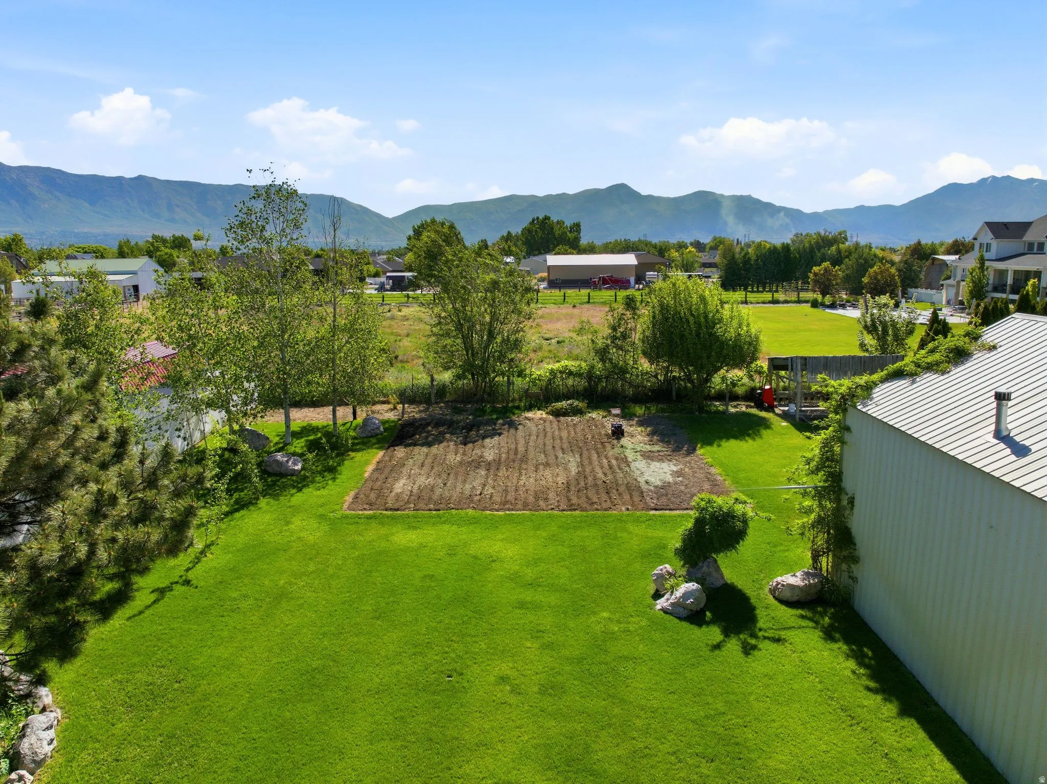 Expansive green lawn with a prepared garden plot, mature trees, and a metal-sided outbuilding