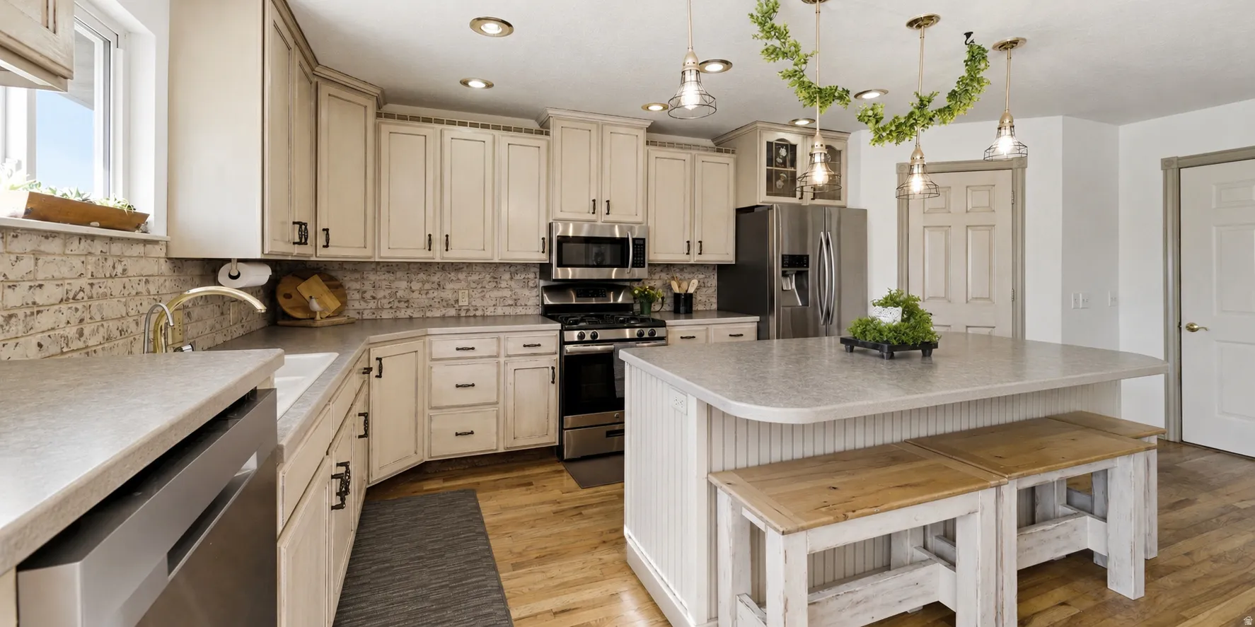 Spacious kitchen featuring light-toned cabinetry, stainless steel appliances, a center island with seating, wood-finish flooring, and a subway tile backsplash