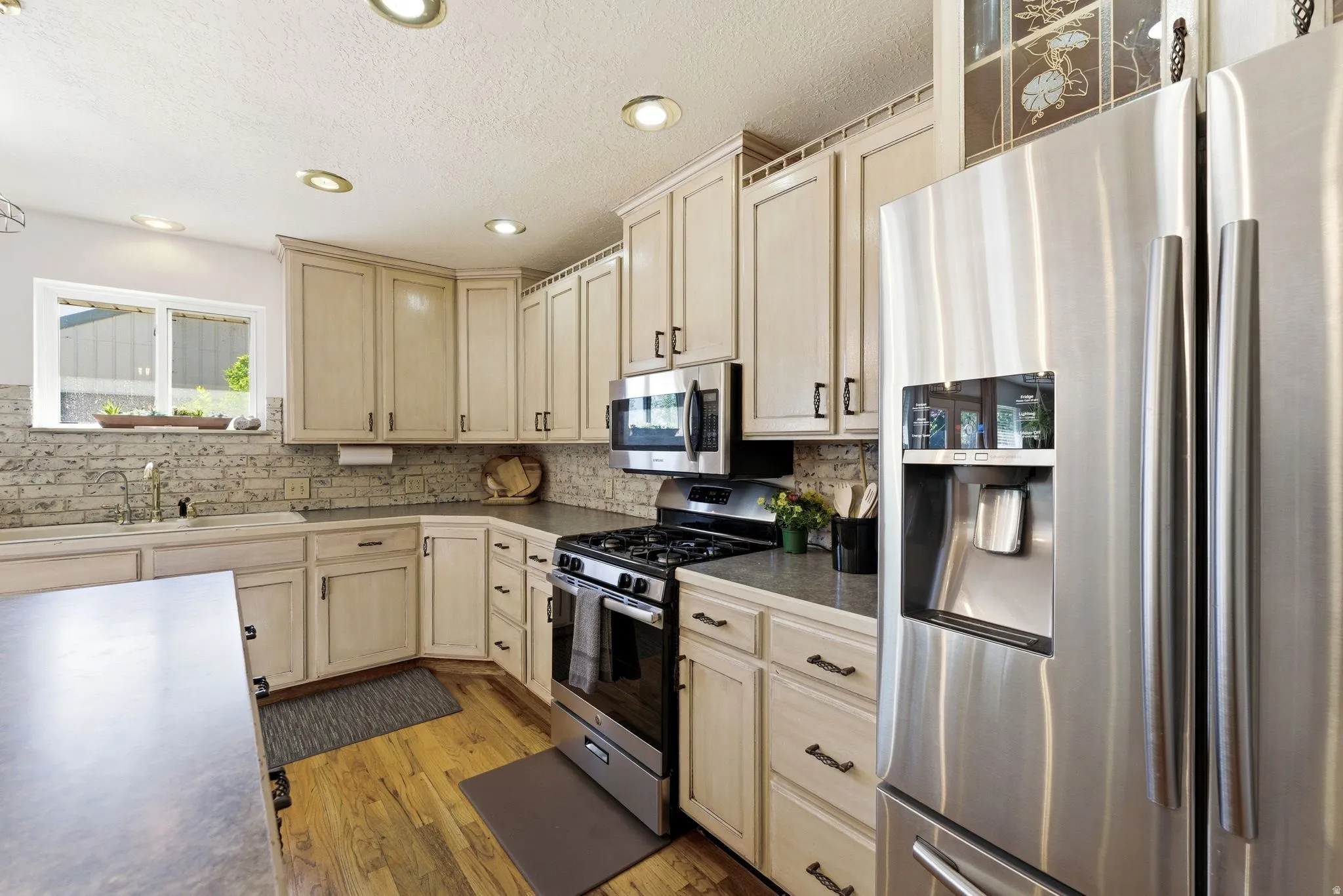 Kitchen featuring light-toned cabinetry, stainless steel appliances, wood-finish flooring, recessed lighting, and a window above the sink