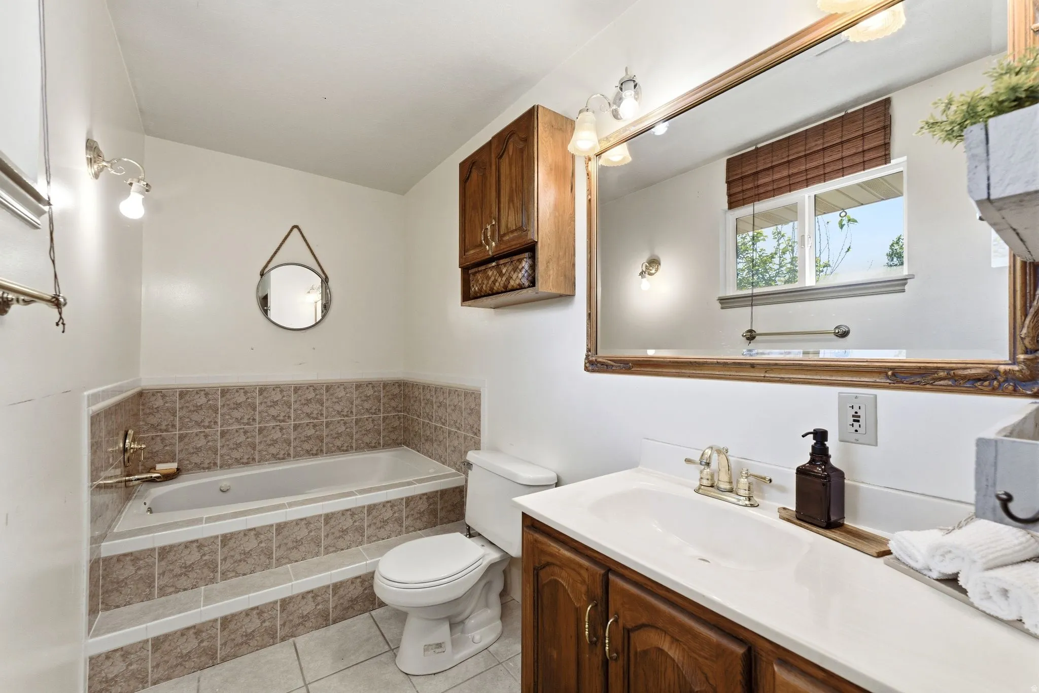 Bathroom featuring a tiled built-in tub, a wood-finish vanity with an integrated sink, a large wall-mounted mirror, and a window with blinds