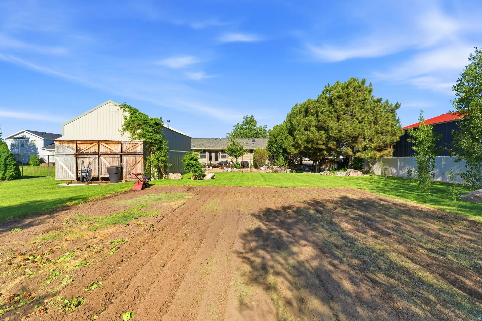 Spacious rear property featuring a cultivated garden area, expansive manicured lawn, an outbuilding with wood doors, and mature landscaping
