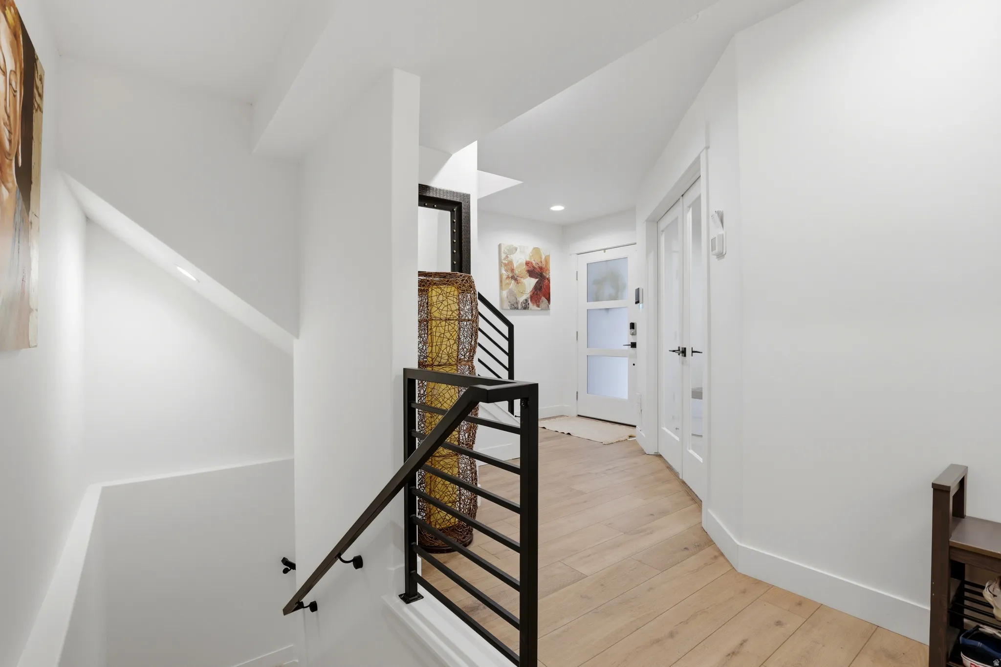 Bright hall with wood-finish flooring, white walls, black metal staircase railing, and frosted glass panel entry door