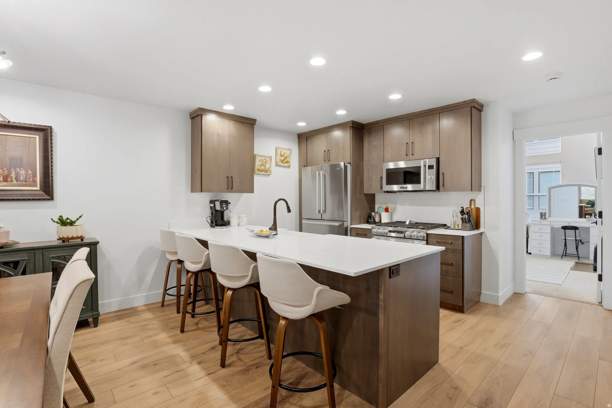 Well-appointed kitchen featuring a substantial island with seating, stainless steel appliances, wood-finish flooring, recessed lighting, and ample cabinetry