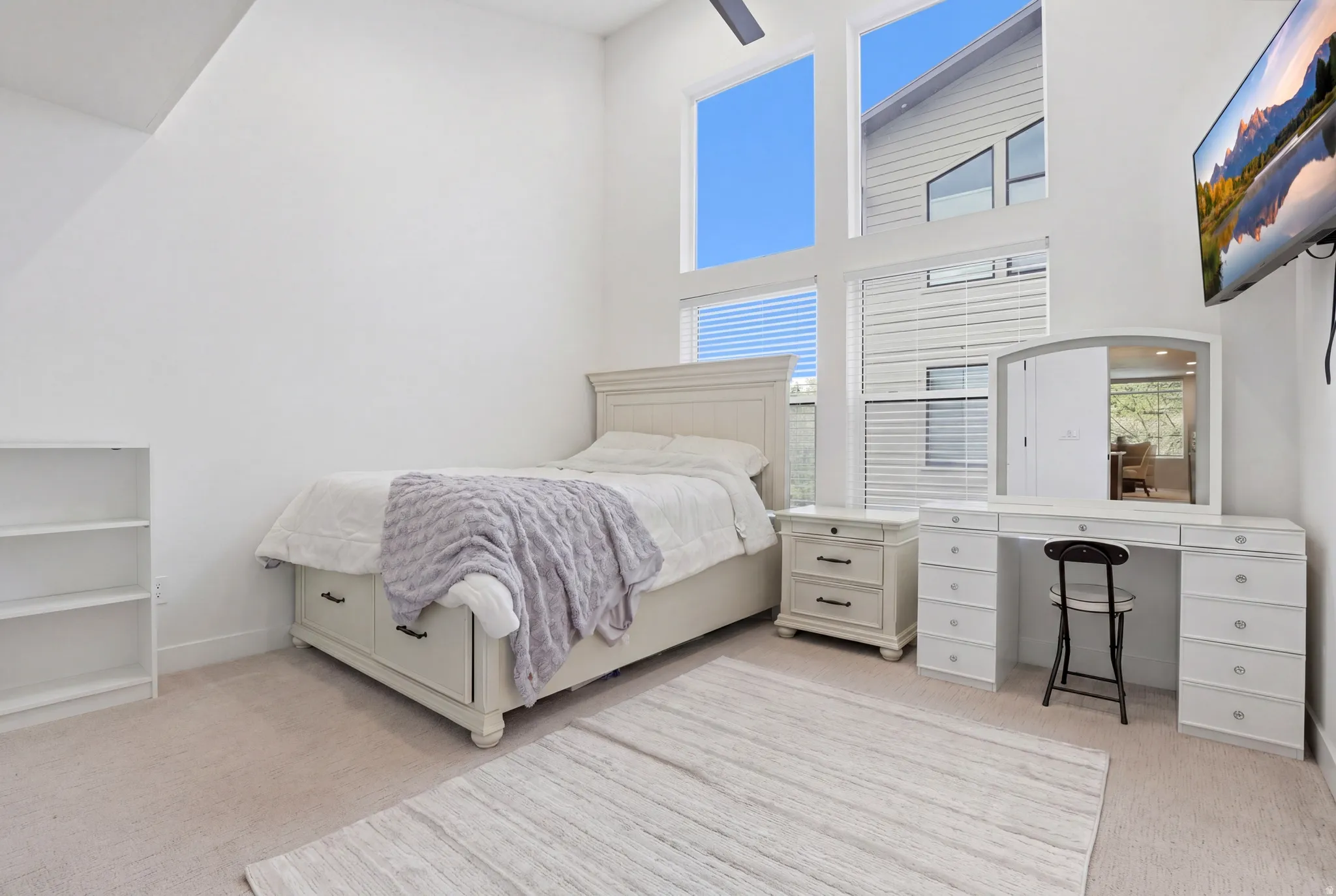 Carpeted room featuring a white upholstered bed frame with built-in storage, a matching nightstand, and a vanity with a tri-fold mirror