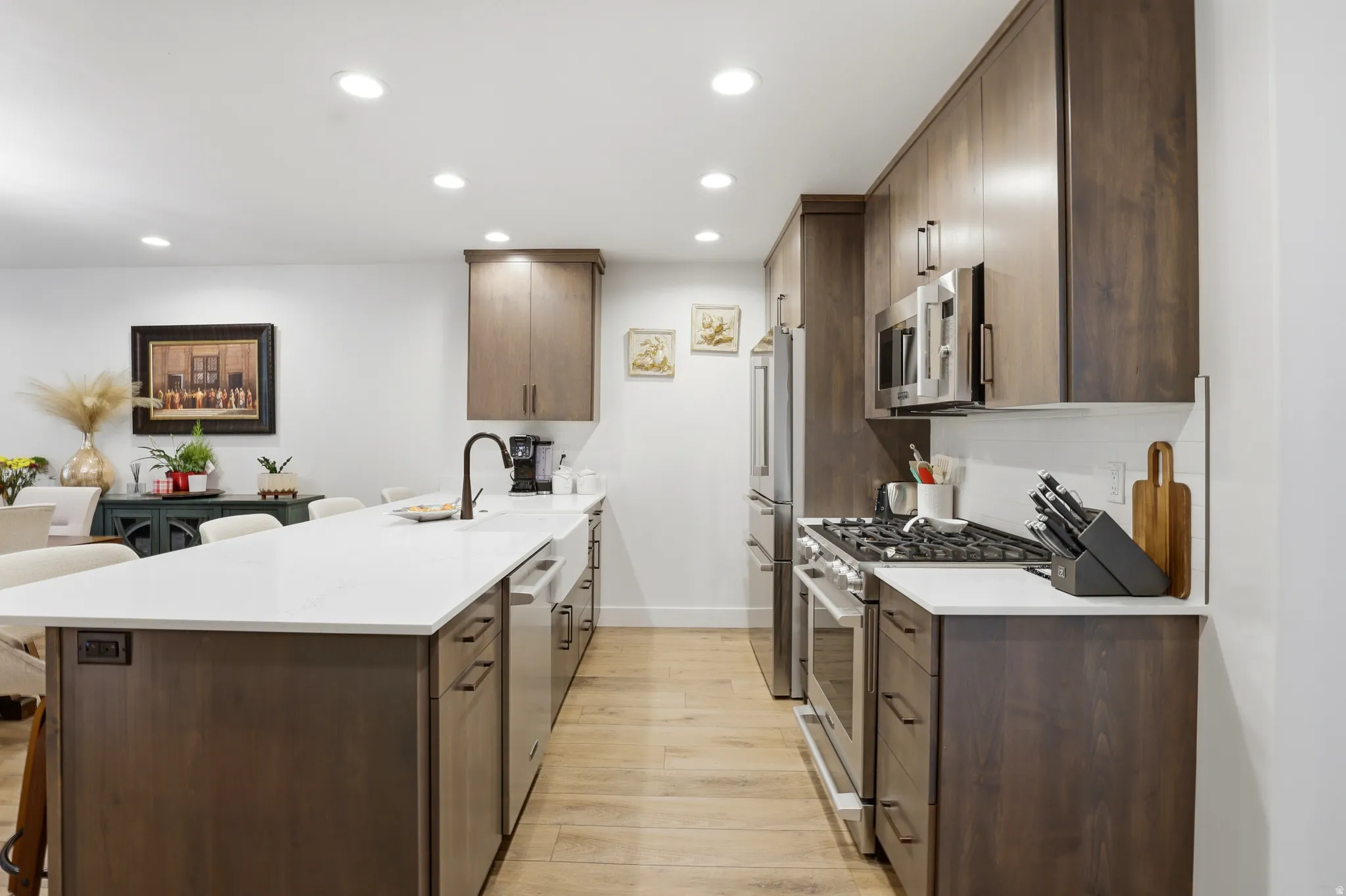 Modern kitchen featuring an expansive center island with a white countertop and seating, wood-finish flooring, stainless steel appliances, and recessed lighting