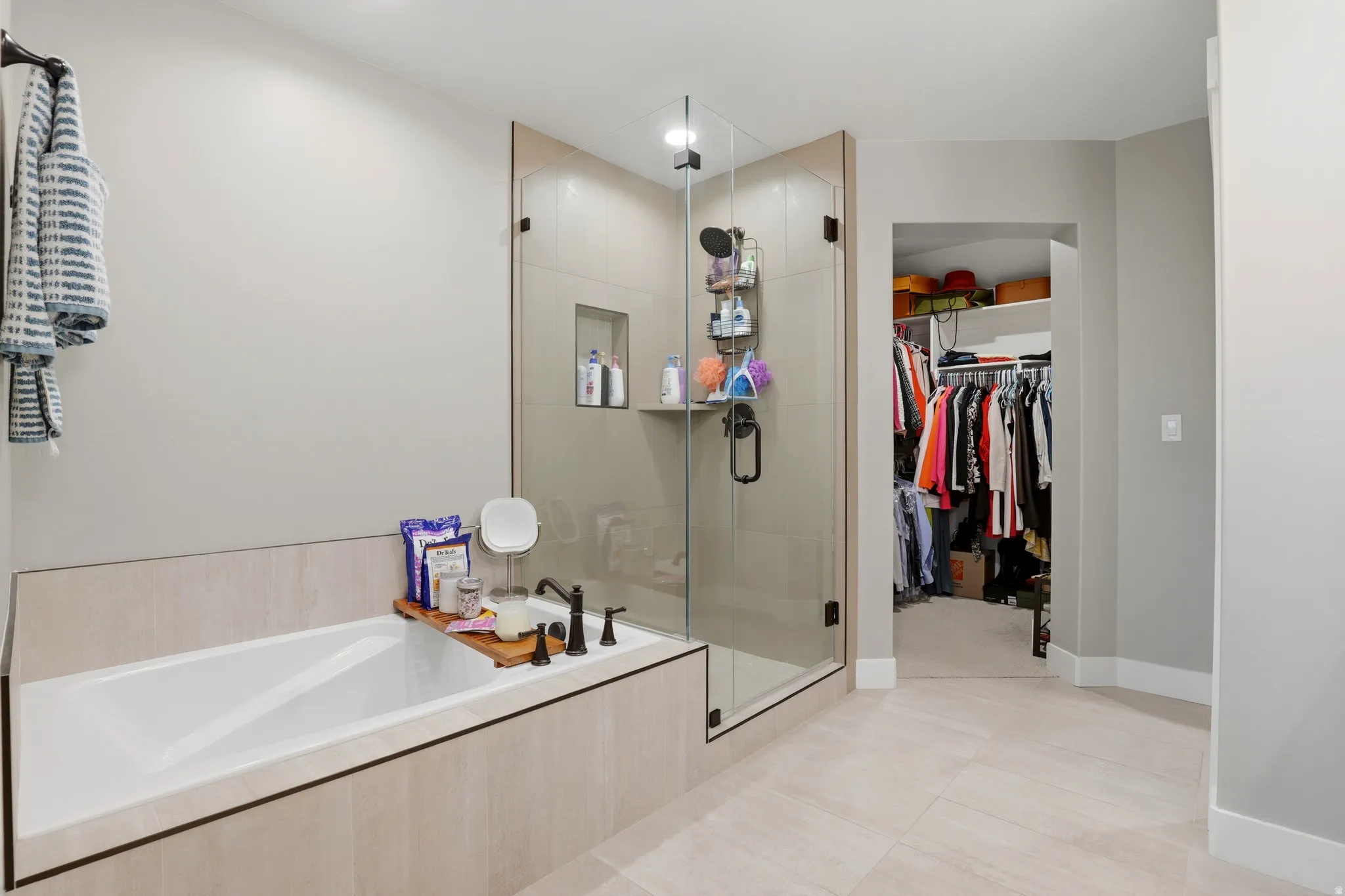 Spacious bathroom featuring a built-in soaking tub with dark bronze fixtures, a frameless glass shower with built-in niche, and large format tile flooring