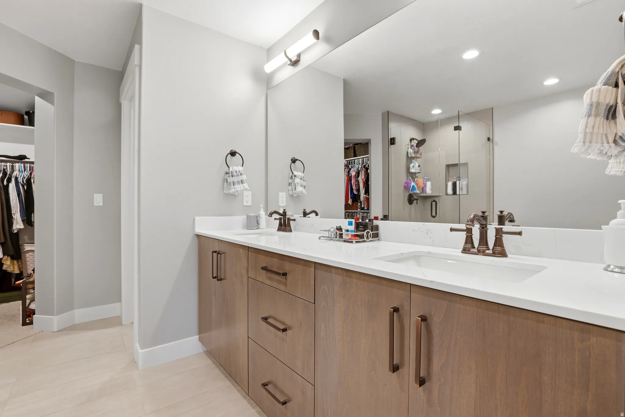 Double vanity featuring light wood-finish cabinetry, white countertops, and bronze-finish fixtures