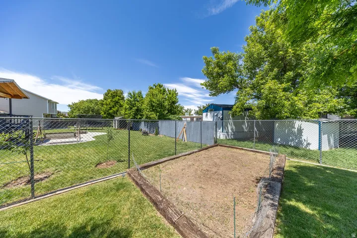 Fenced backyard featuring a large garden bed with wood borders, manicured lawn, and mature trees