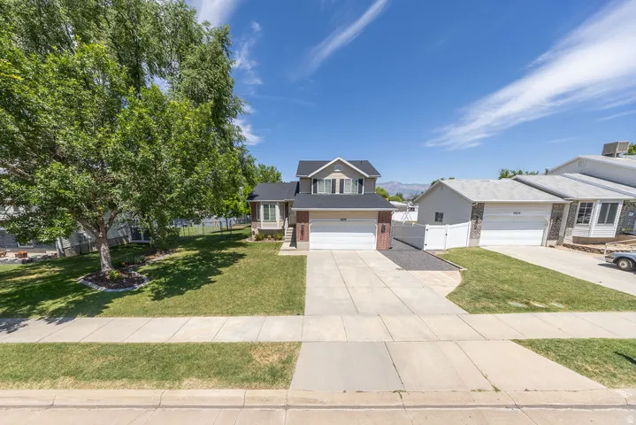 Two-story residence featuring a two-car garage, concrete driveway, and a front lawn with mature trees