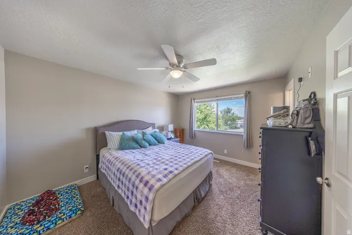 Spacious room featuring neutral painted walls, textured carpet flooring, a ceiling fan with integrated lighting, and a large window with natural light