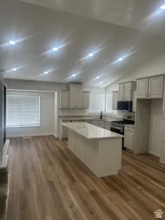 Open-concept kitchen and living area featuring vaulted ceilings with recessed lighting, wood-finish flooring, a central island with a light-toned countertop, and light-colored cabinetry