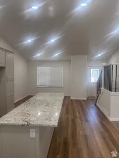 Kitchen island with a light-toned countertop, wood-finish flooring, recessed lighting, and a partial view of a staircase with black metal balusters