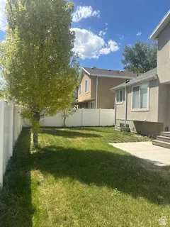 Fenced backyard featuring a mature tree, green lawn, and a concrete patio