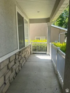 Covered front porch featuring a stone veneer accent wall, stucco siding, and white railing