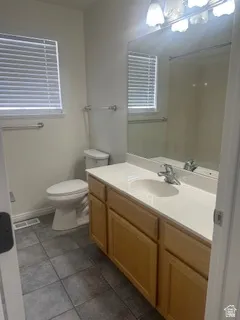 Bathroom featuring a single vanity with a white countertop, light wood-finish cabinetry, an integrated sink, a large mirror, and tiled flooring