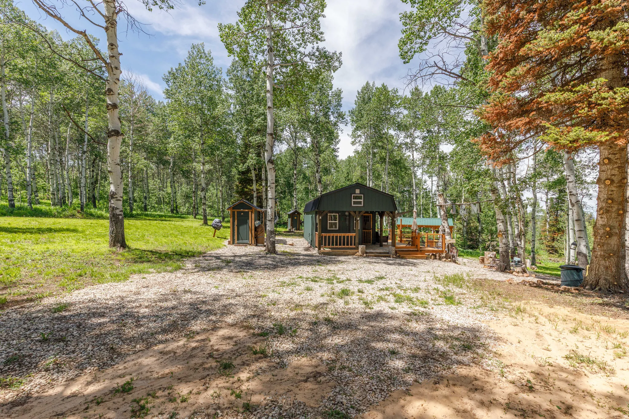 Wooded property featuring a dark green cabin with a covered porch and wood railing