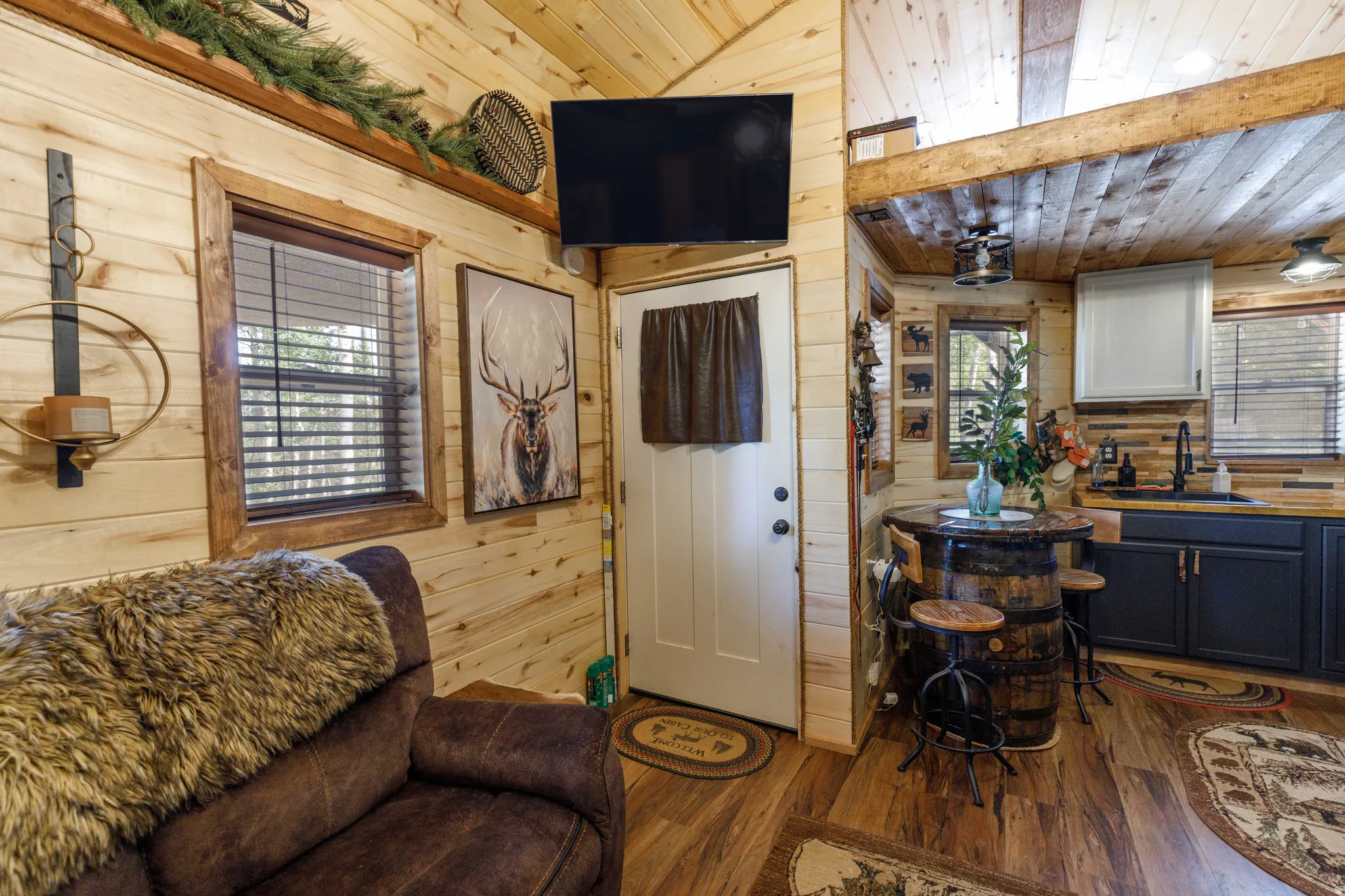 Natural wood-finish wall paneling throughout, featuring a functional kitchen area with dark cabinetry, integrated sink, and wood-finish countertops