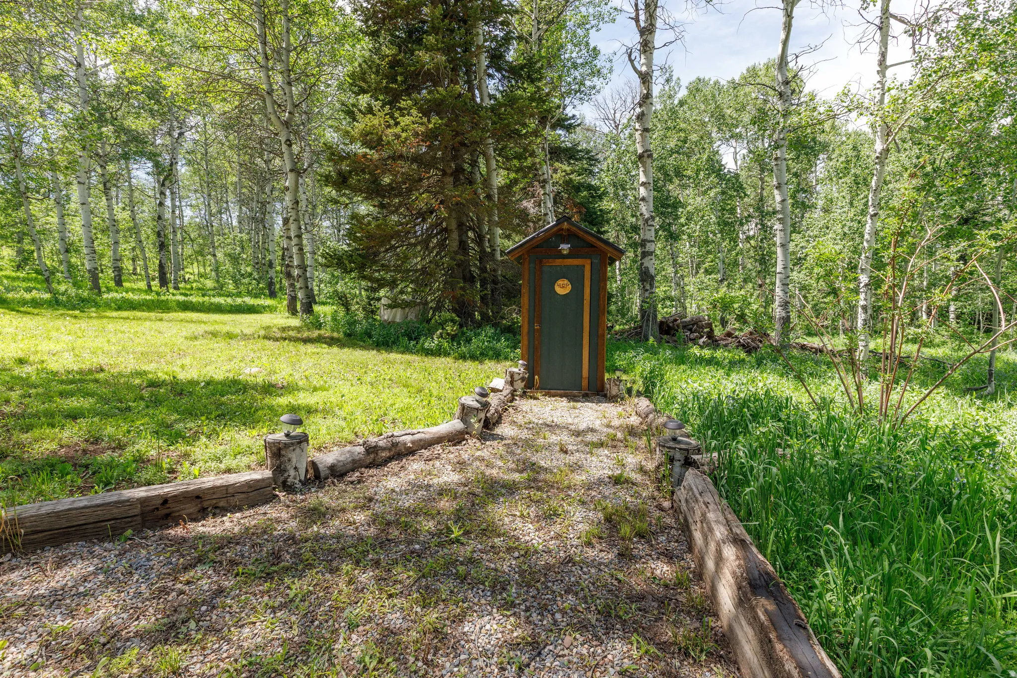 Wood-sided outhouse with a dark green door, set on a gravel path