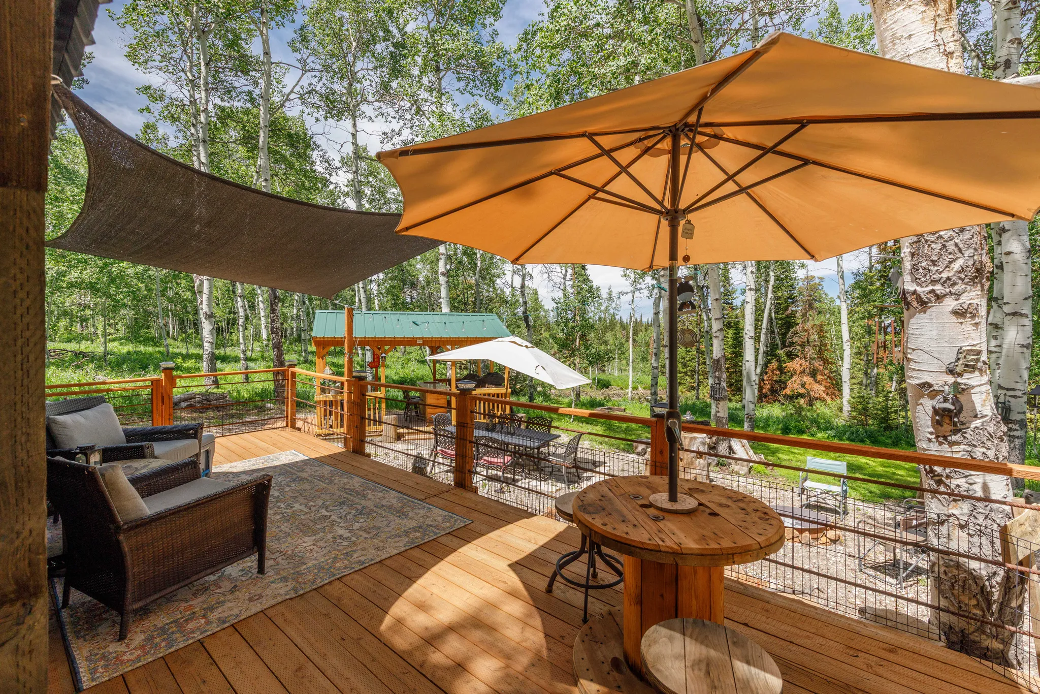 Expansive wooden deck with a shade sail, cable railing, and a rustic wood spool table