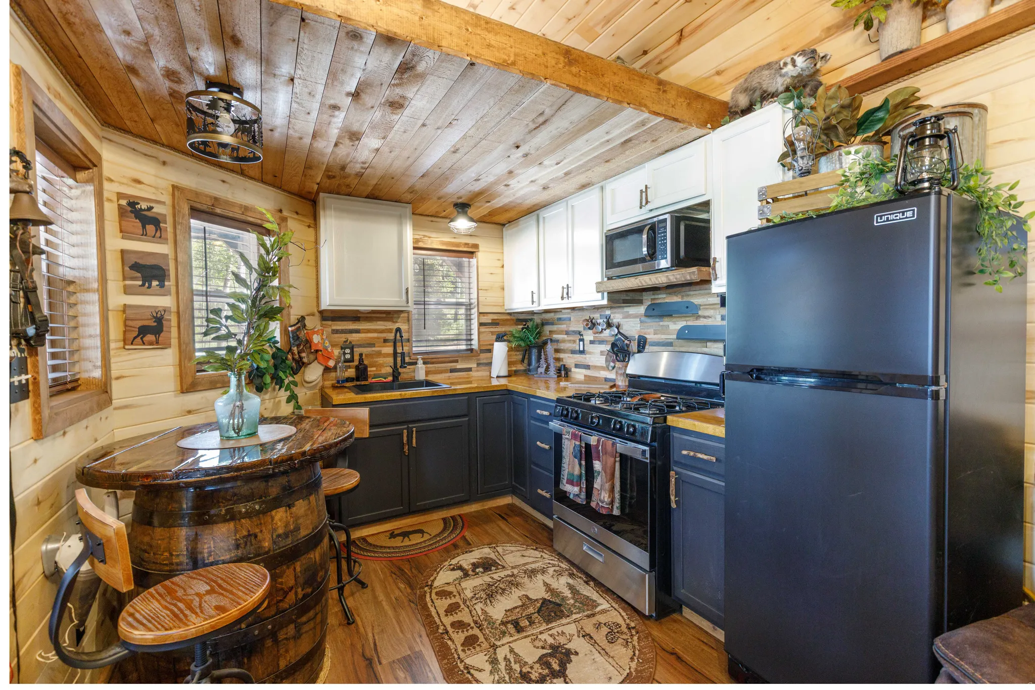 Kitchen featuring natural wood-finish walls and ceiling, two-tone cabinetry with white upper and dark lower units, wood-finish countertops, and stainless steel appliances