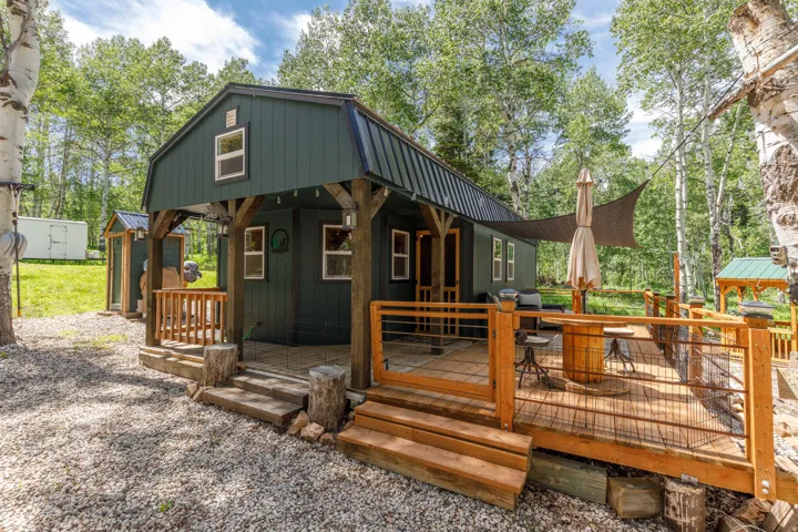 Dark green barn-style dwelling featuring a covered porch with exposed timber framing and a spacious wood deck
