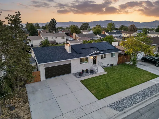 Contemporary single-family residence featuring a dark shingle roof with integrated solar panels, a light-colored exterior, and a dark brown garage door