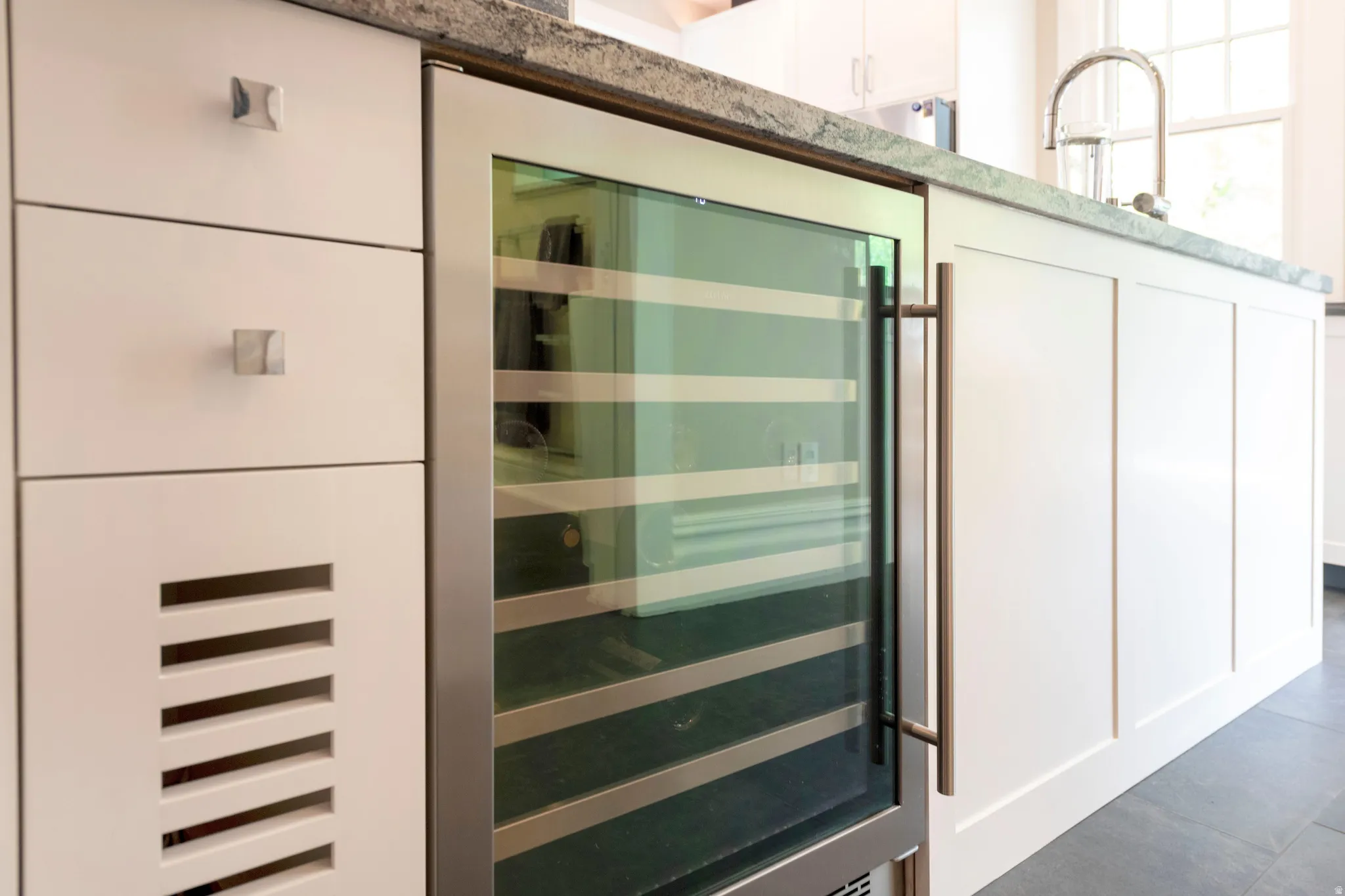 Integrated beverage refrigerator with a glass-front door, brushed metal hardware, white cabinetry, and a stone countertop