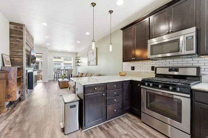 Contemporary kitchen featuring dark wood cabinetry, light-toned countertops, stainless steel appliances, and a white subway tile backsplash