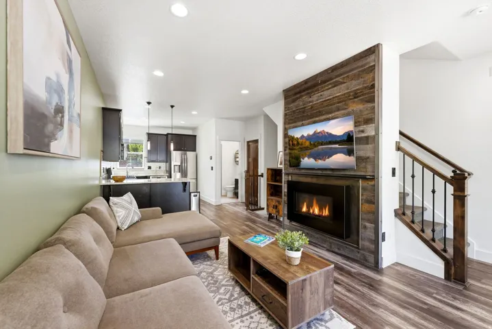 Living area featuring a floor-to-ceiling wood-paneled fireplace, wood-finish flooring, recessed lighting, and a staircase with dark wood handrails and black metal balusters