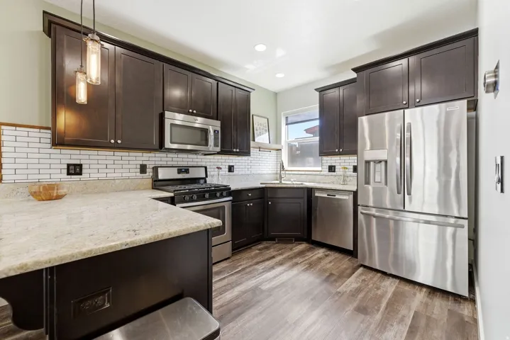 Kitchen featuring dark wood cabinetry, light-toned countertops, subway tile backsplash, stainless steel appliances, and wood-finish flooring