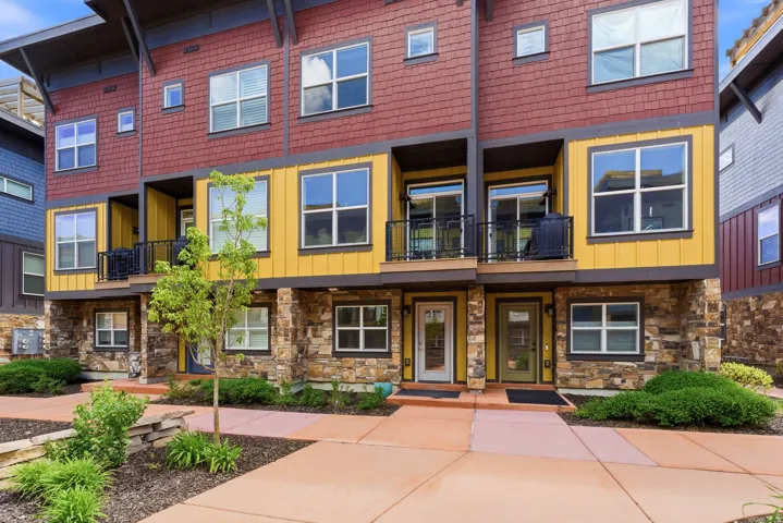 Contemporary townhome exterior featuring stone accents on the lower level, vibrant yellow siding on the middle floor, and red cedar shake siding on the upper level