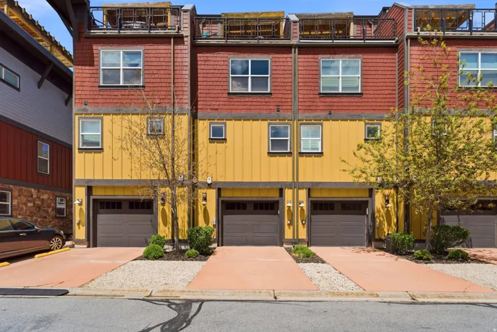 Modern townhome architecture featuring a multi-level design, individual garage access, private driveways, and a rooftop deck