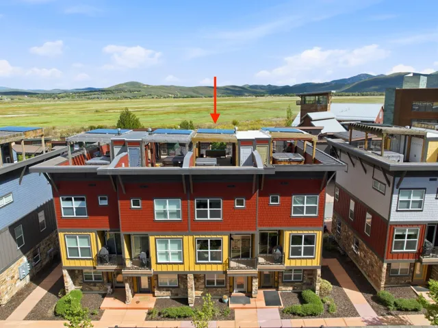 Modern townhome exterior featuring multi-level siding in red and yellow hues, ground-floor stone accents, and private balconies