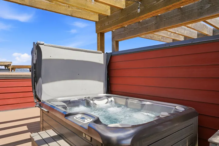 Rooftop hot tub with bubbling water, set against red horizontal siding and an overhead wooden pergola