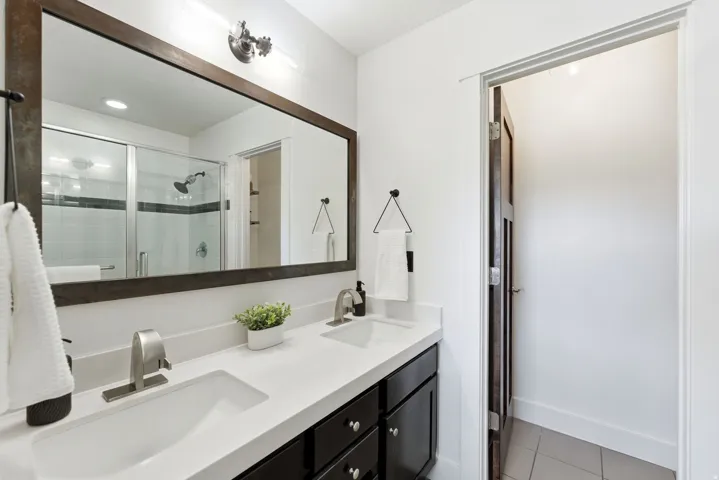 Bathroom vanity featuring dual under-mount sinks with brushed nickel faucets, a white countertop, and dark wood-finish cabinetry