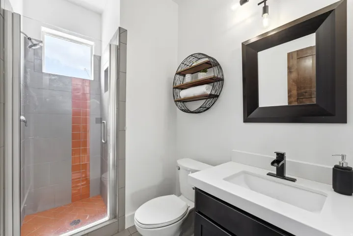Modern bathroom featuring a walk-in shower with a glass enclosure, gray and orange tile accents, and a window for natural light