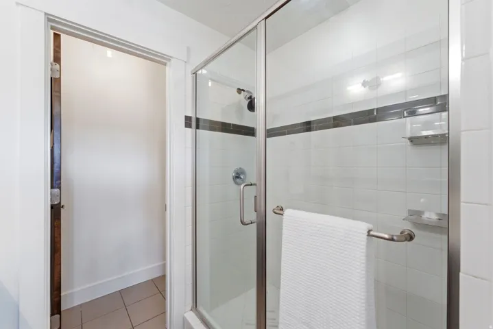 Glass-enclosed shower featuring white subway tile, a dark accent tile band, and polished chrome fixtures