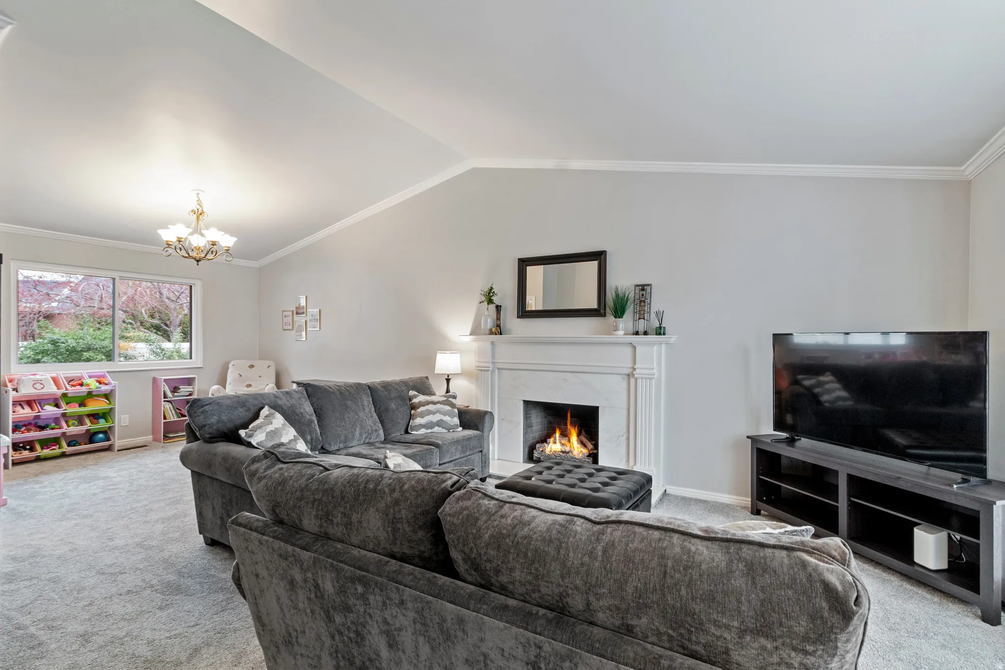 Living room featuring a vaulted ceiling, light grey carpeting, and a fireplace with a white mantel and surround
