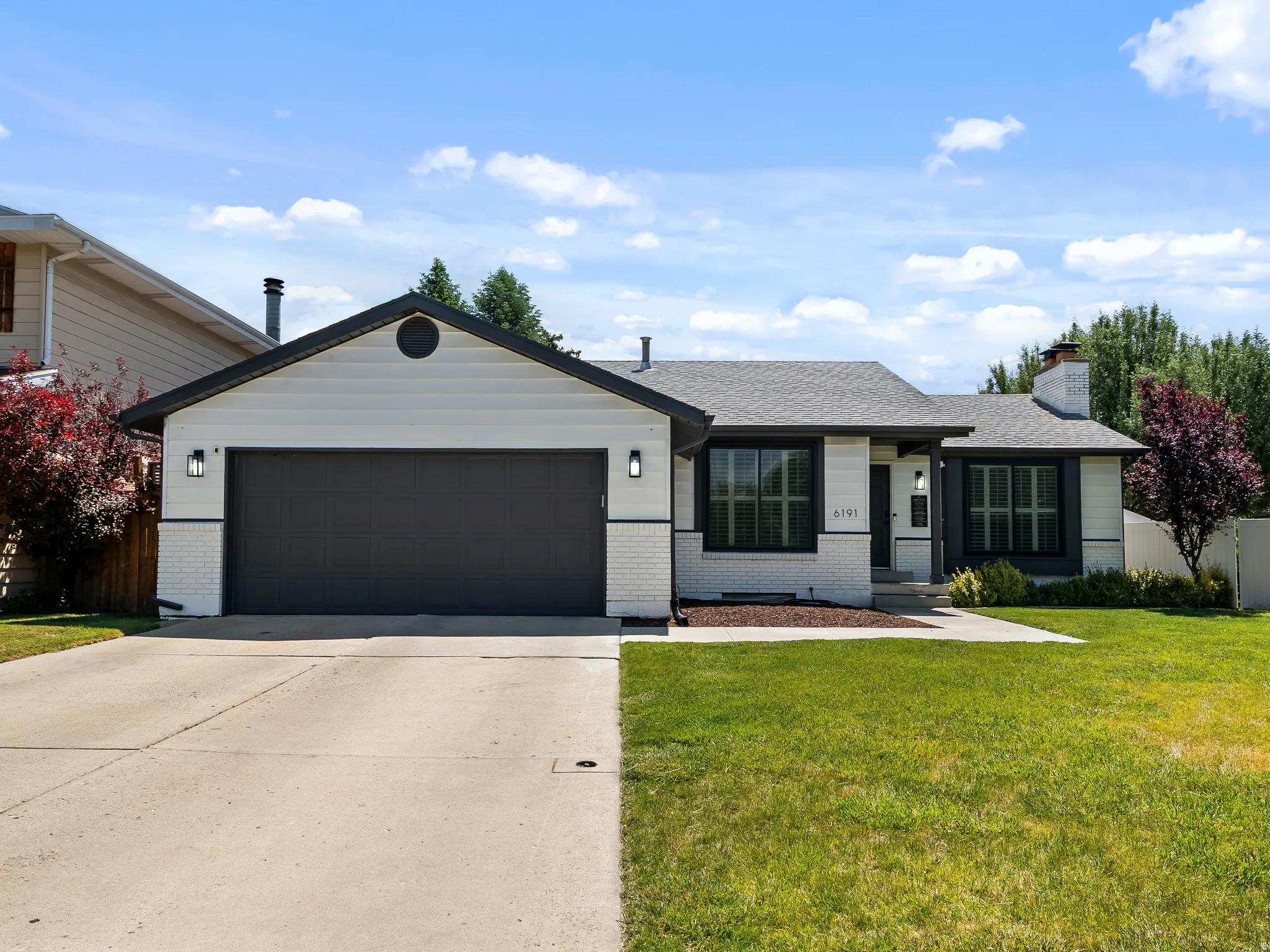 Single-story residence featuring a two-car garage, white brick and siding exterior, dark trim accents, and a concrete driveway