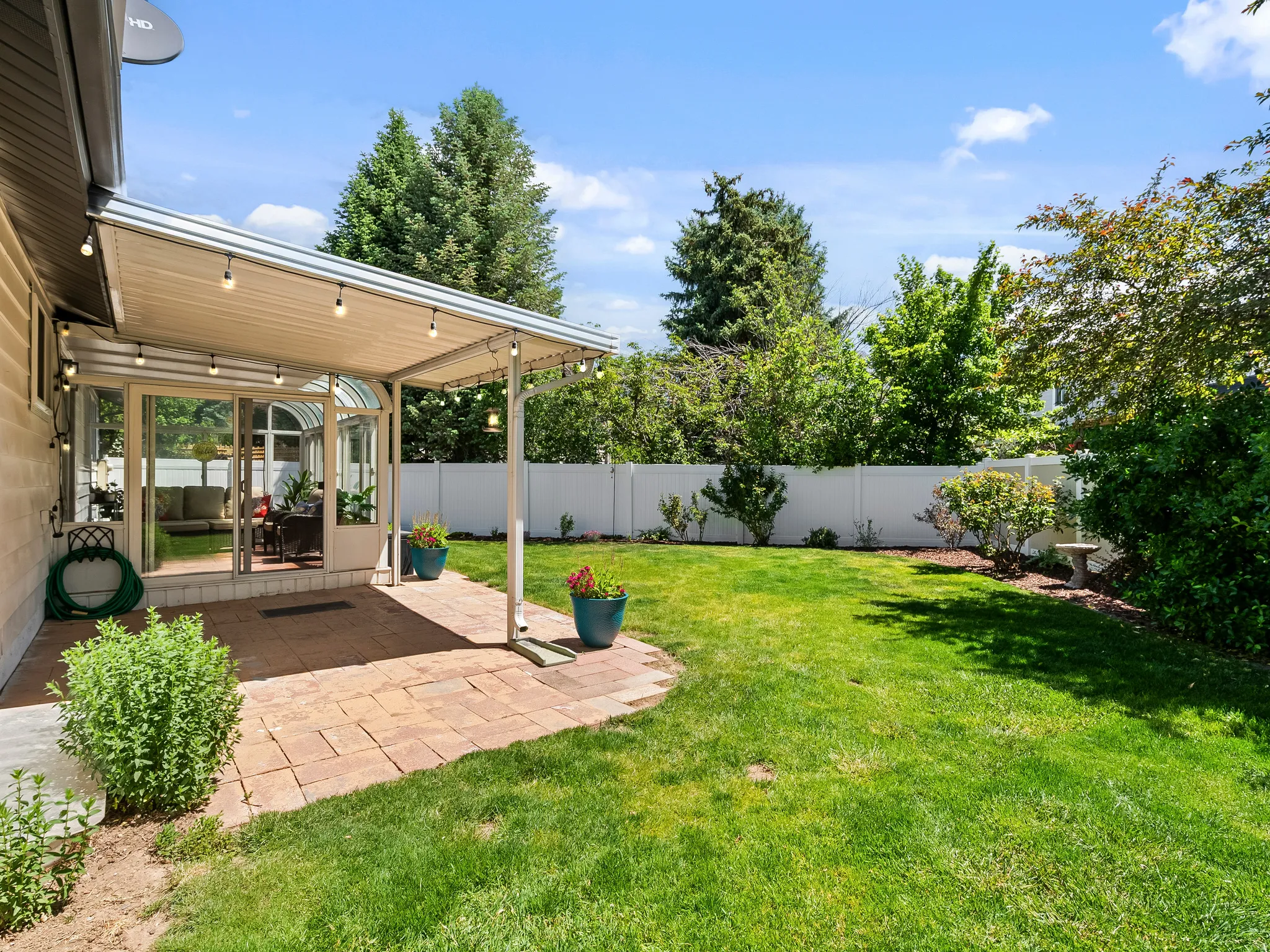 Expansive backyard featuring a manicured lawn, white privacy fencing, and mature trees