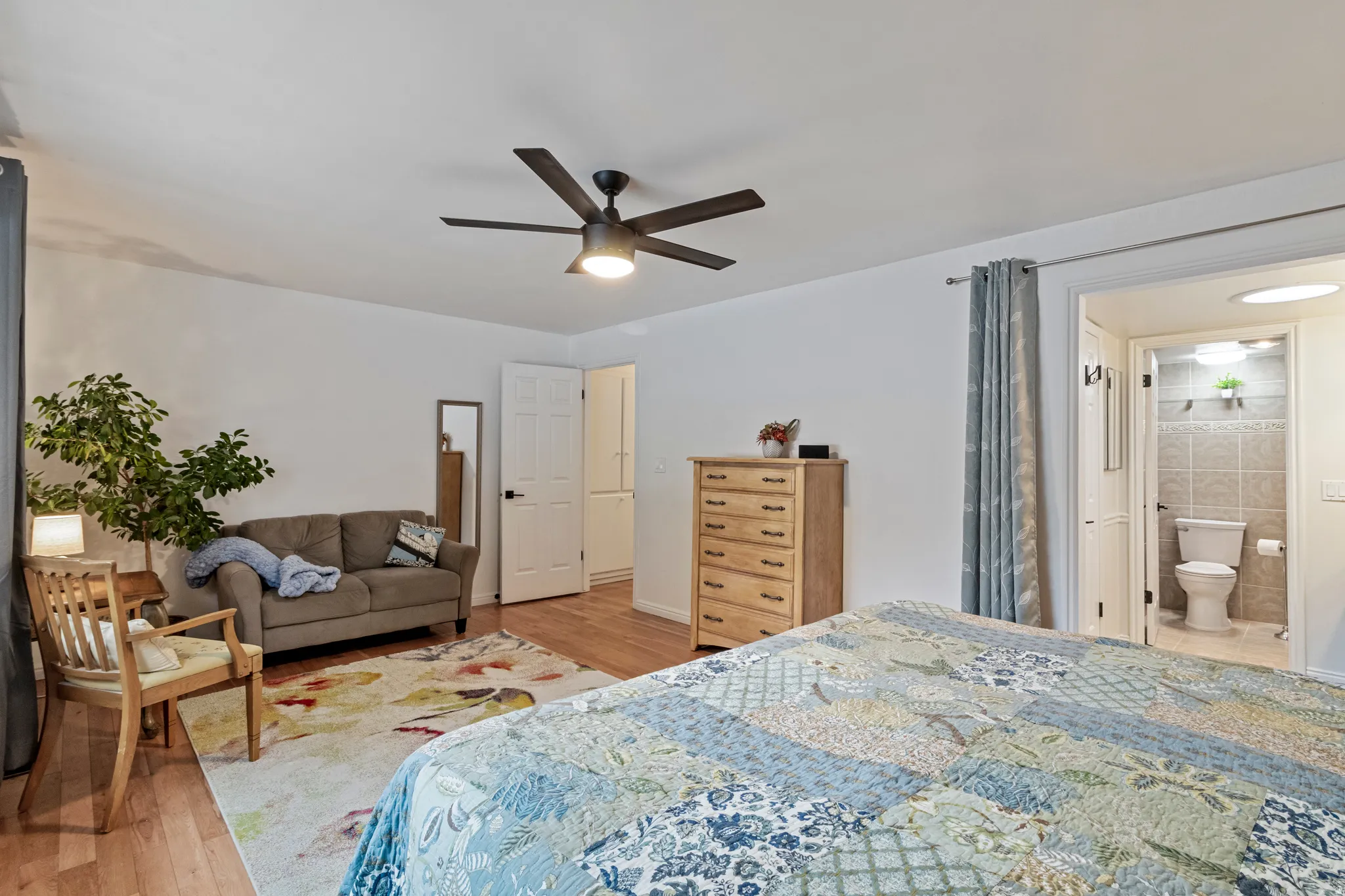 Spacious bedroom featuring wood-finish flooring, a contemporary ceiling fan with integrated lighting, and an ensuite bathroom entry