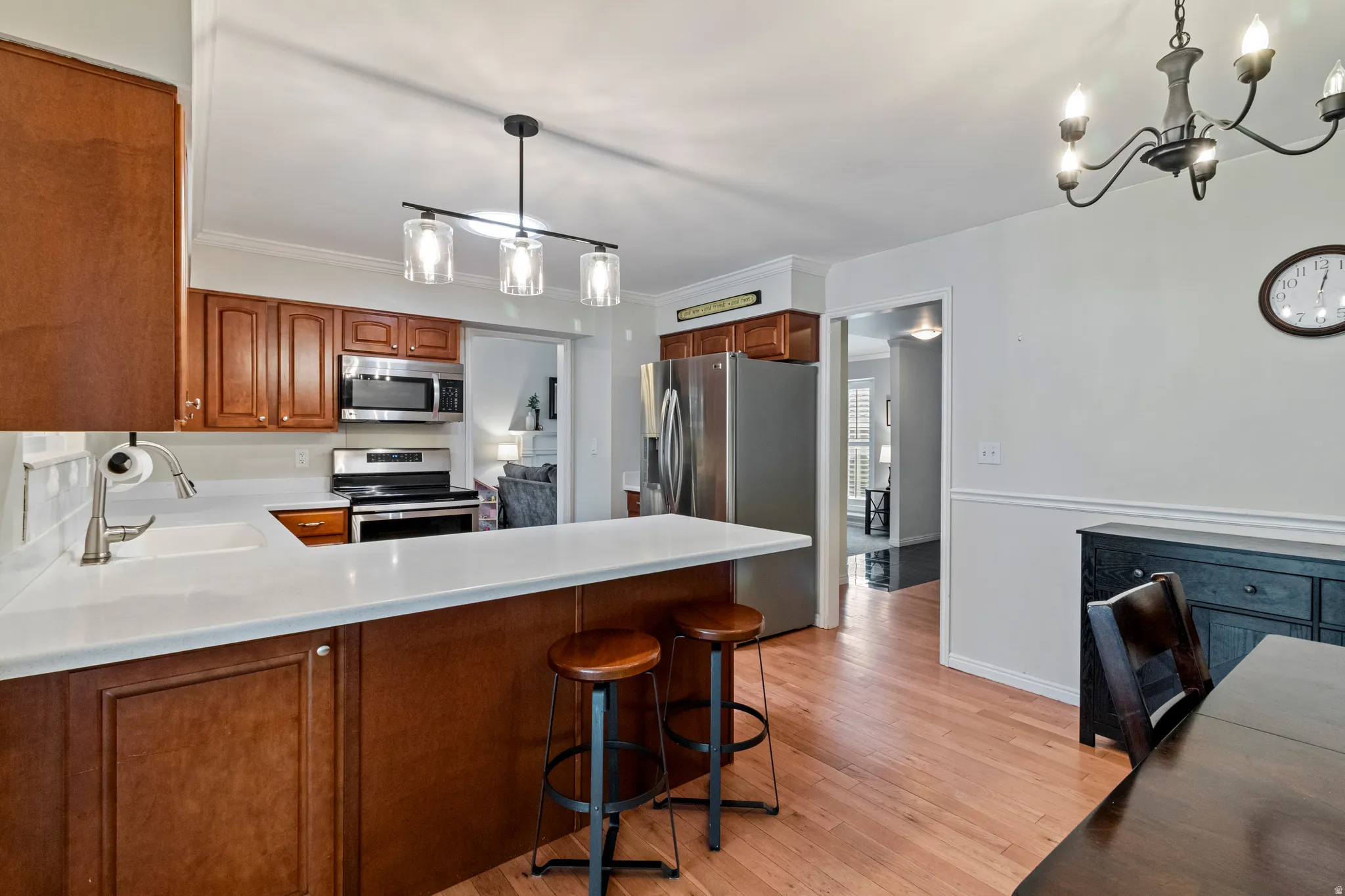 Kitchen featuring wood-finish cabinetry, stainless steel appliances, a white solid surface countertop, and wood-finish flooring