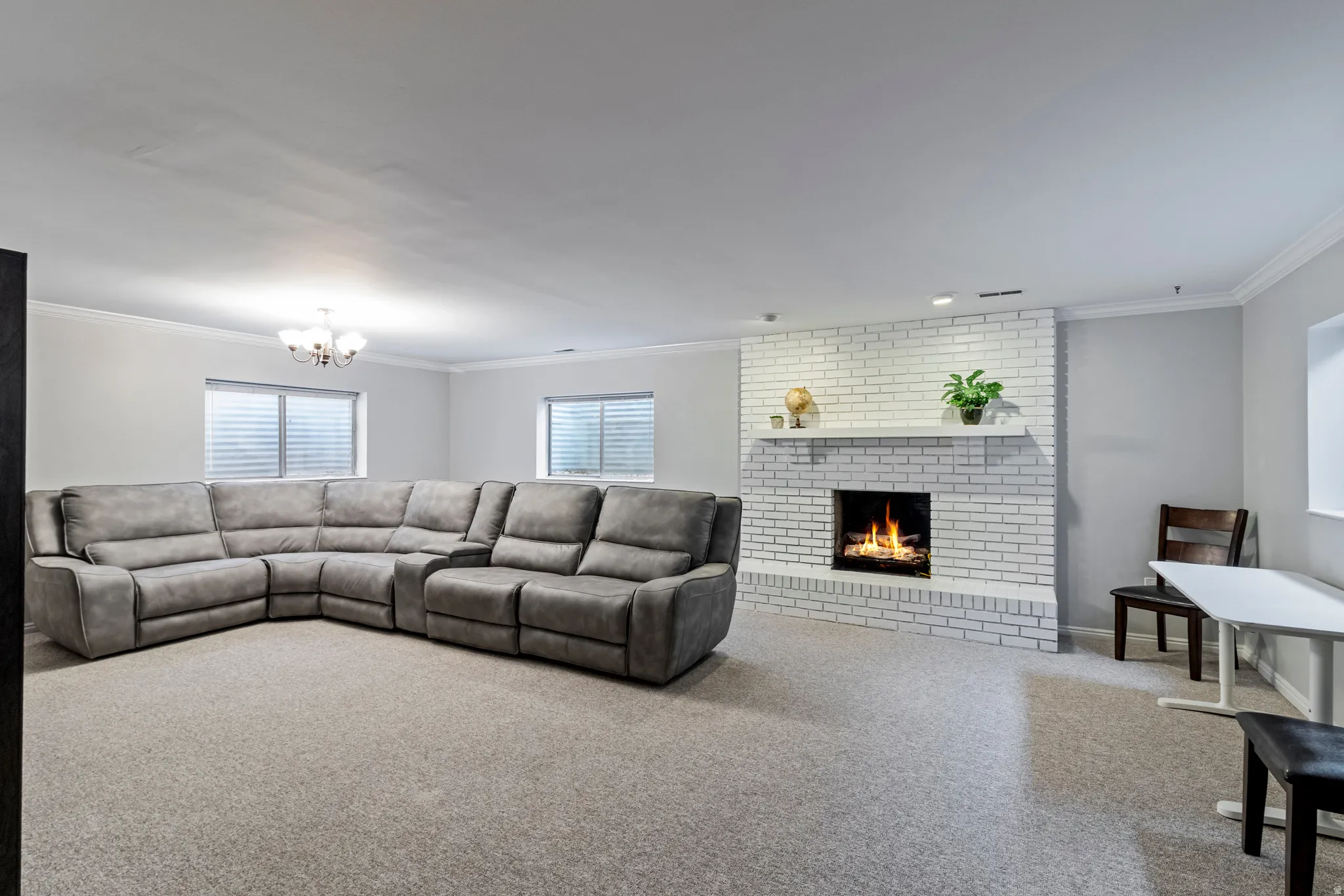 Spacious room featuring a white brick fireplace with mantel, recessed lighting, crown molding, and two windows with blinds