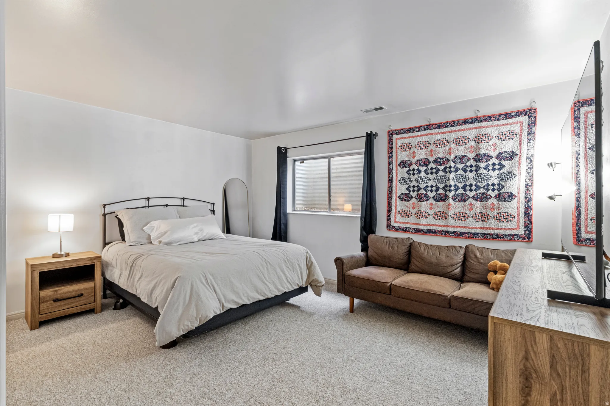 Spacious room featuring light-colored carpeting, a window with horizontal blinds, and dark curtains