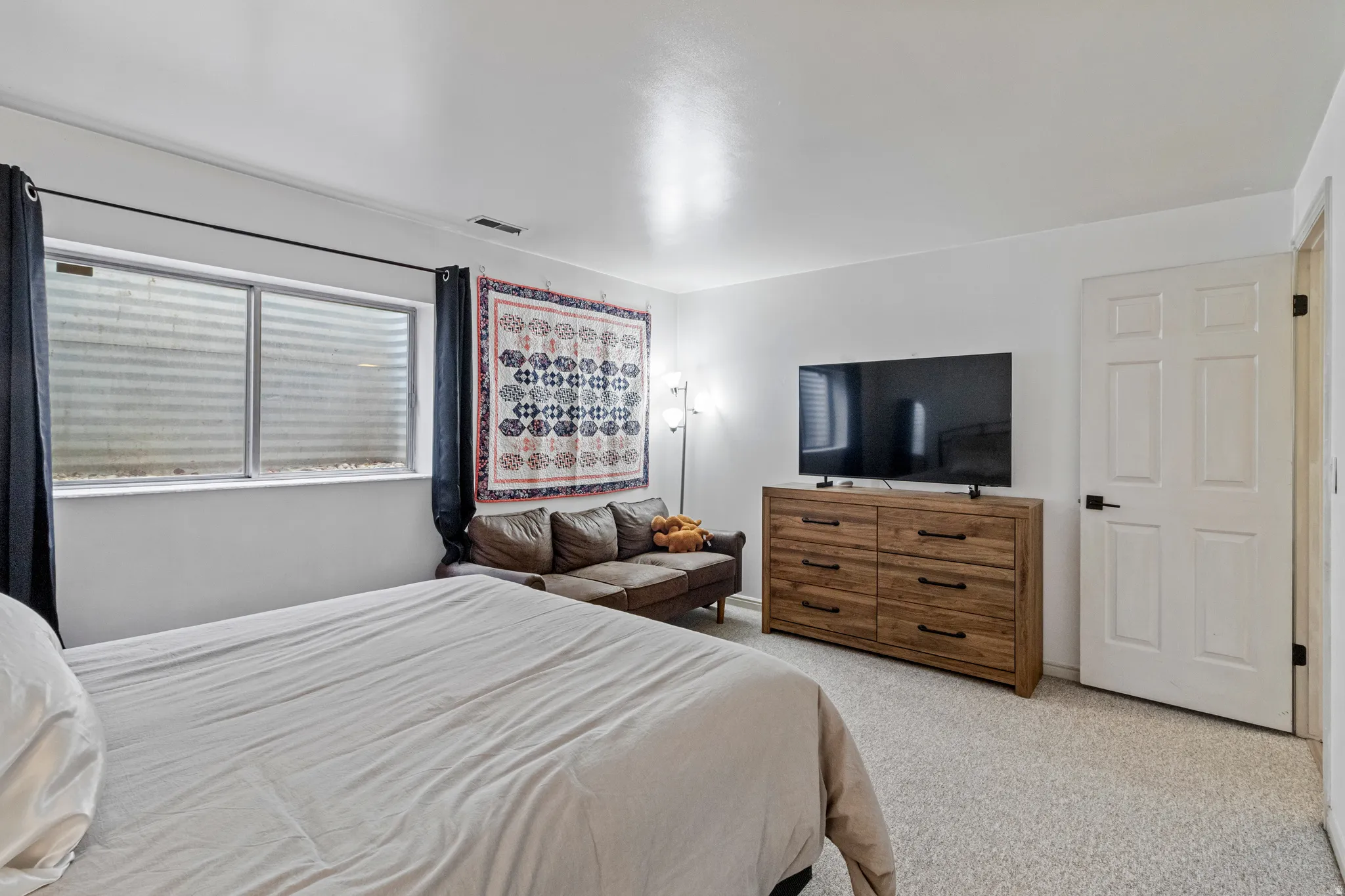 Bright room featuring wall-to-wall carpeting, a multi-pane window, and a white six-panel door with matte black hardware