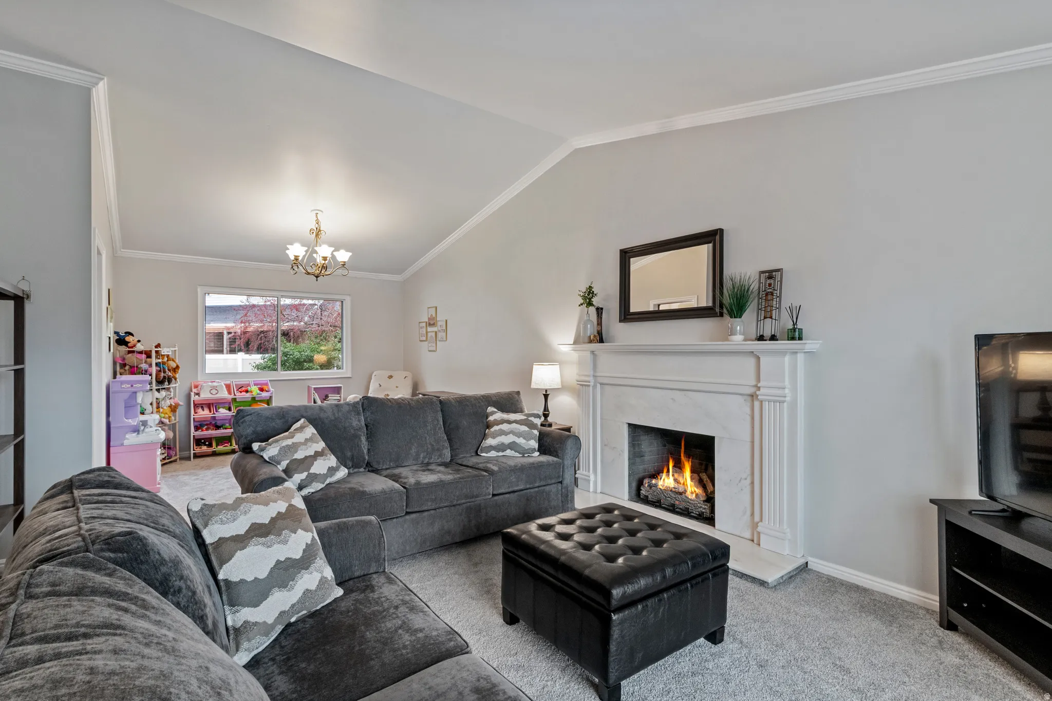 Living area featuring a vaulted ceiling with crown molding, a built-in fireplace with a stone surround, a chandelier, and a large window